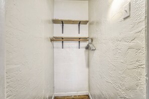 Un couloir étroit aux murs blancs et au plancher en bois. Deux étagères en bois sont fixées au mur, et chacune est dotée d’un crochet en métal.