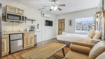 A compact living space with a kitchenette, a bed, a seating area, and a ceiling fan.