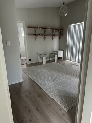 A spacious room with a large grey rug, wooden flooring, a glass-top table, and a white cabinet. - Modern house with three bedrooms (Vestfold)