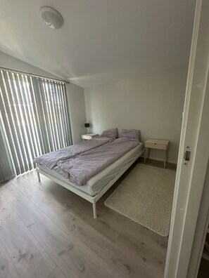 A bedroom with a bed, bedside tables, a nightstand, a window with blinds, and a light fixture. - Modern house with three bedrooms (Vestfold)