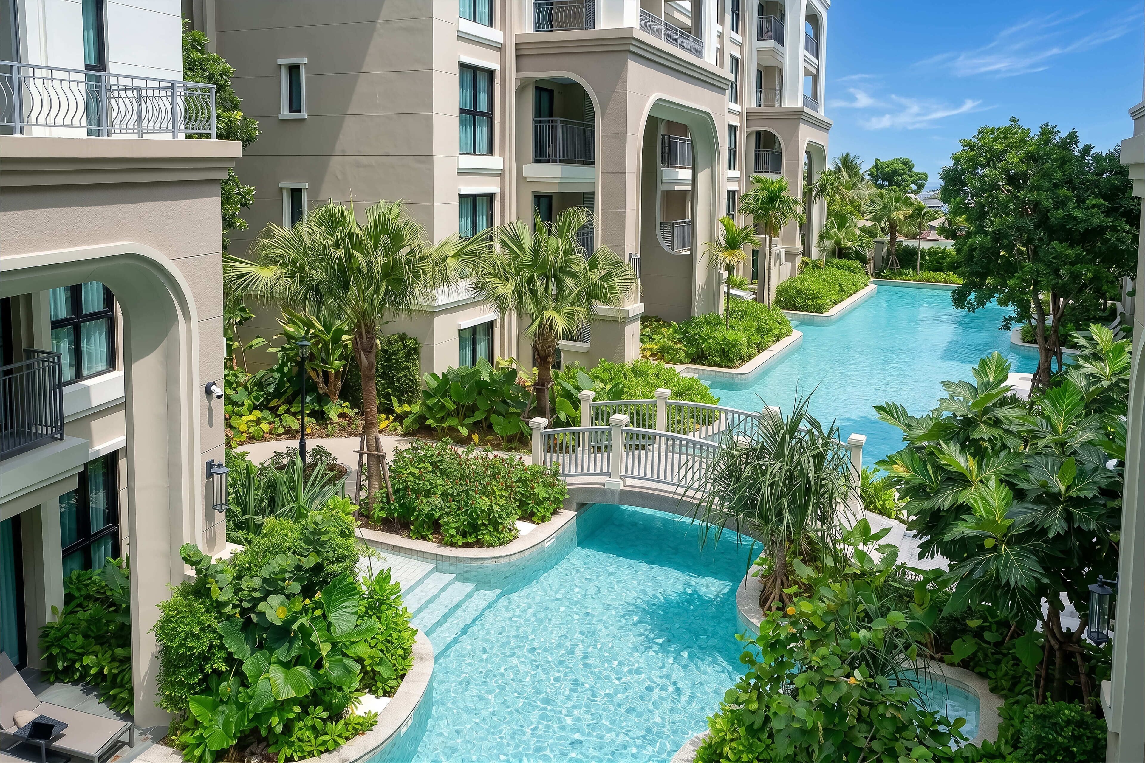 A multi-level hotel with a central swimming pool surrounded by lush greenery and palm trees.