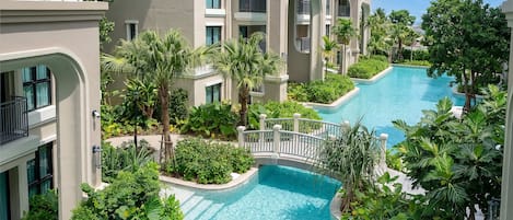 A multi-level hotel with a central swimming pool surrounded by lush greenery and palm trees.