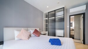 A modern hotel room with a large bed, a wardrobe, and a built-in air conditioning unit.