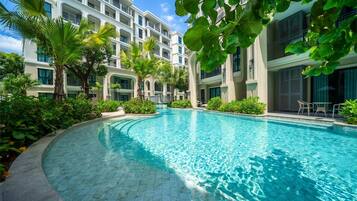Una piscina rodeada de exuberante vegetación y un edificio de varios pisos con balcones.