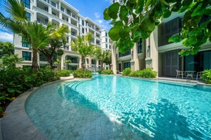 A swimming pool surrounded by lush greenery and a multi-story building with balconies. - Title Legendary D606 (Tambon Choeng Thale)