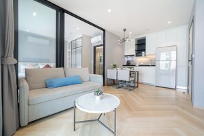 A modern living room with a sofa, a coffee table, and a kitchen area with a dining table and chairs. - Title Legendary D606 (Tambon Choeng Thale)