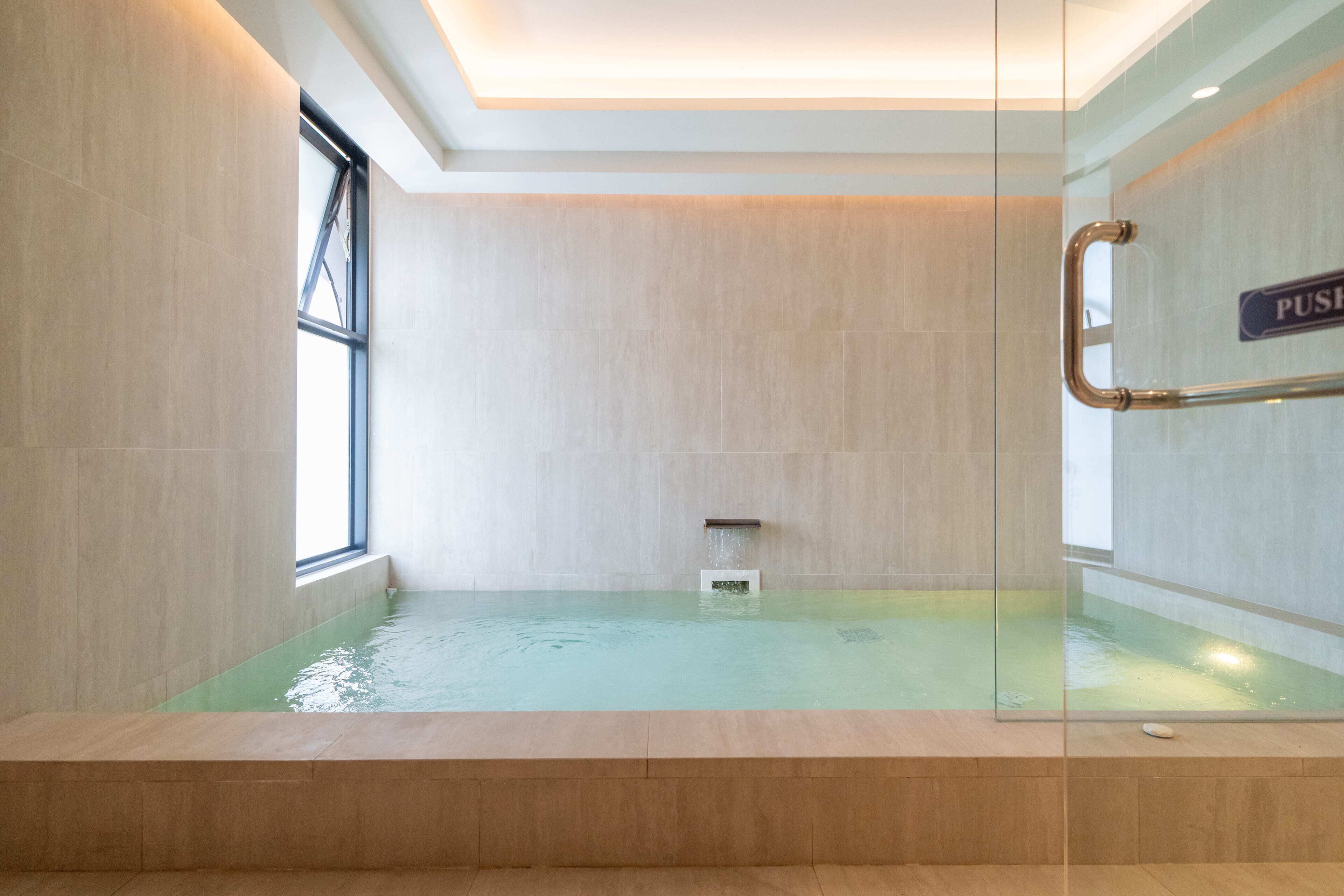 Un baño moderno con un jacuzzi de vidrio, una ventana y una barra de empuje.