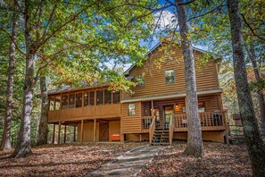 A two-story log cabin with a deck, surrounded by trees. - DogWood Lodge - Hot Tub, Near Kerith House Winery (Morganton)