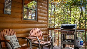 A wooden cabin with a deck, two Adirondack chairs, a grill, and a propane tank. - DogWood Lodge with Hot Tub (Morganton)