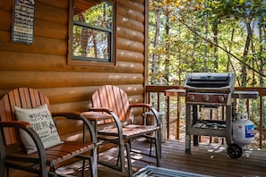 Eine Holzhütte mit einer Veranda, zwei Adirondack-Stühlen, einem Grill und einem Propangasbehälter.