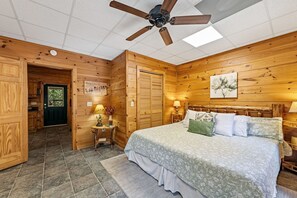 A wooden-paneled bedroom with a bed, bedside lamps, a ceiling fan, and a door leading to a bathroom. - DogWood Lodge - Hot Tub, Near Kerith House Winery (Morganton)