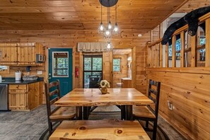 Ein Holzhütten-Interieur mit Esstisch, Stühlen, einer Kandelaber und einer Küchenzeile.