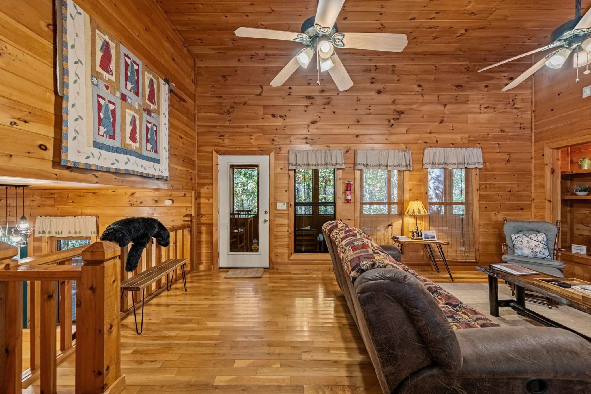Interior d'una cabana de fusta amb una zona de seients central, un ventilador de sostre i una porta que dona a una altra habitació.