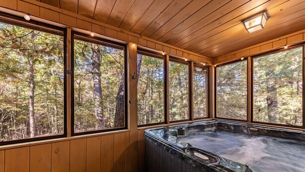 A wooden cabin with a hot tub and large windows overlooking a forest. - DogWood Lodge with Hot Tub (Morganton)