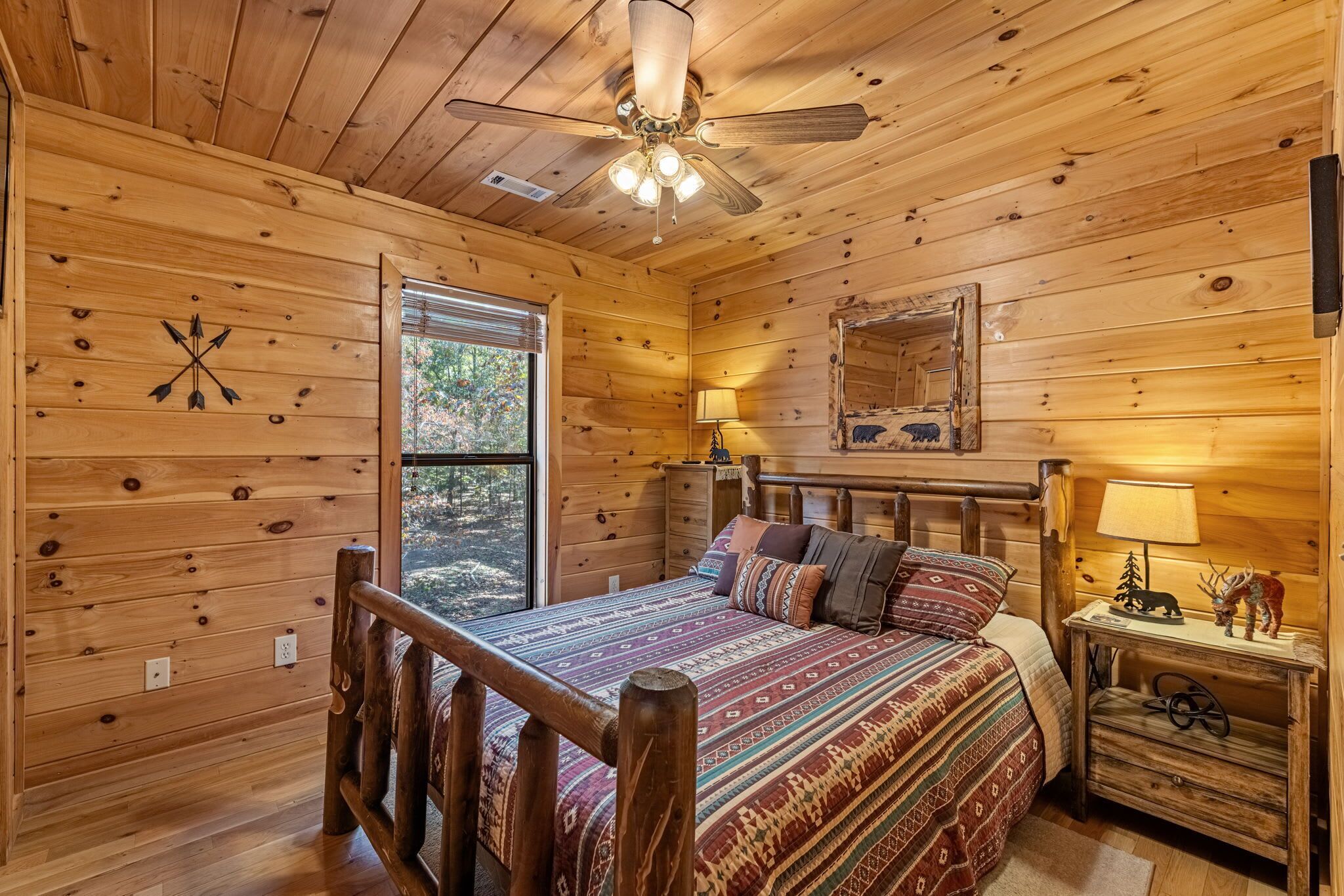 A wooden cabin bedroom with a bed, bedside table, lamp, and a ceiling fan.