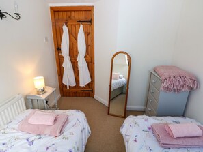 Un dormitorio con dos camas, una puerta de madera, un espejo, un aparador y una lámpara de noche.