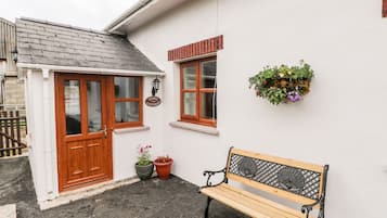Une petite maison blanche avec une porte et une fenêtre en bois, un banc et des plantes en pot.