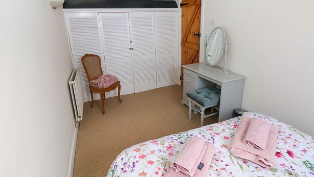 A bedroom with a bed, a chair, a dresser, a mirror, and a wardrobe. - The Stable (Haverfordwest)