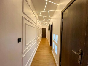 A hallway with a wooden floor, white walls, and a dark wooden door. - Premium 2-Bedroom Apartment | Luxury, Comfort & Convenience (Lagos)