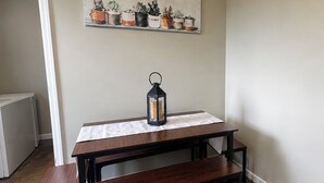 Ein Holztisch mit einer Bank, einer Laterne und einem an der Wand befestigten Regal mit Blumentöpfen.