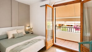 Un dormitorio con cama, mesita de noche, lámpara y vista a un balcón con barandilla.
