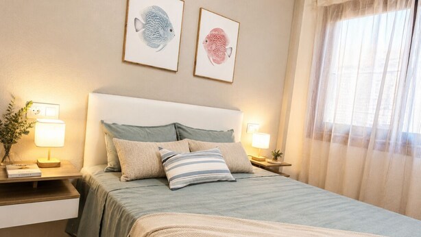 Un dormitorio con cama, almohadas, mesitas de noche, lámparas y una obra de arte con peces en la pared.