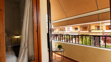 Un balcon donnant sur un immeuble doté de balcons, une petite table avec une plante et un rideau partiellement tiré.