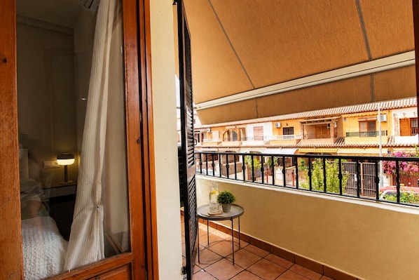 A balcony with a view of a building with balconies, a small table with a plant, and a curtain partially drawn.