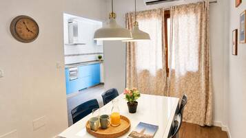Un coin repas avec une table dressée pour deux personnes, une horloge et une vue sur la cuisine.
