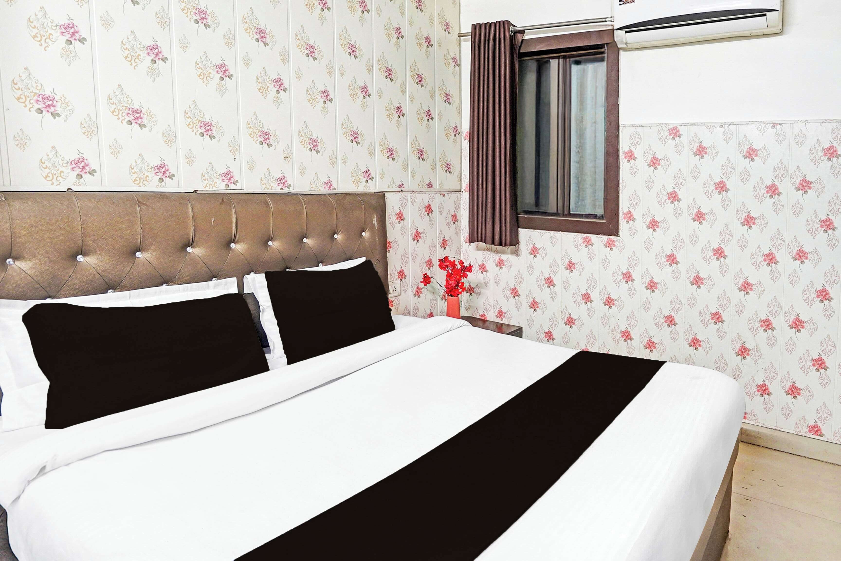Ett hotellrum med en säng, blommig tapet, ett fönster med gardiner och en luftkonditioneringsanläggning.