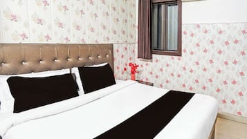 Ett hotellrum med en säng, blommig tapet, ett fönster med gardiner och en luftkonditioneringsanläggning.