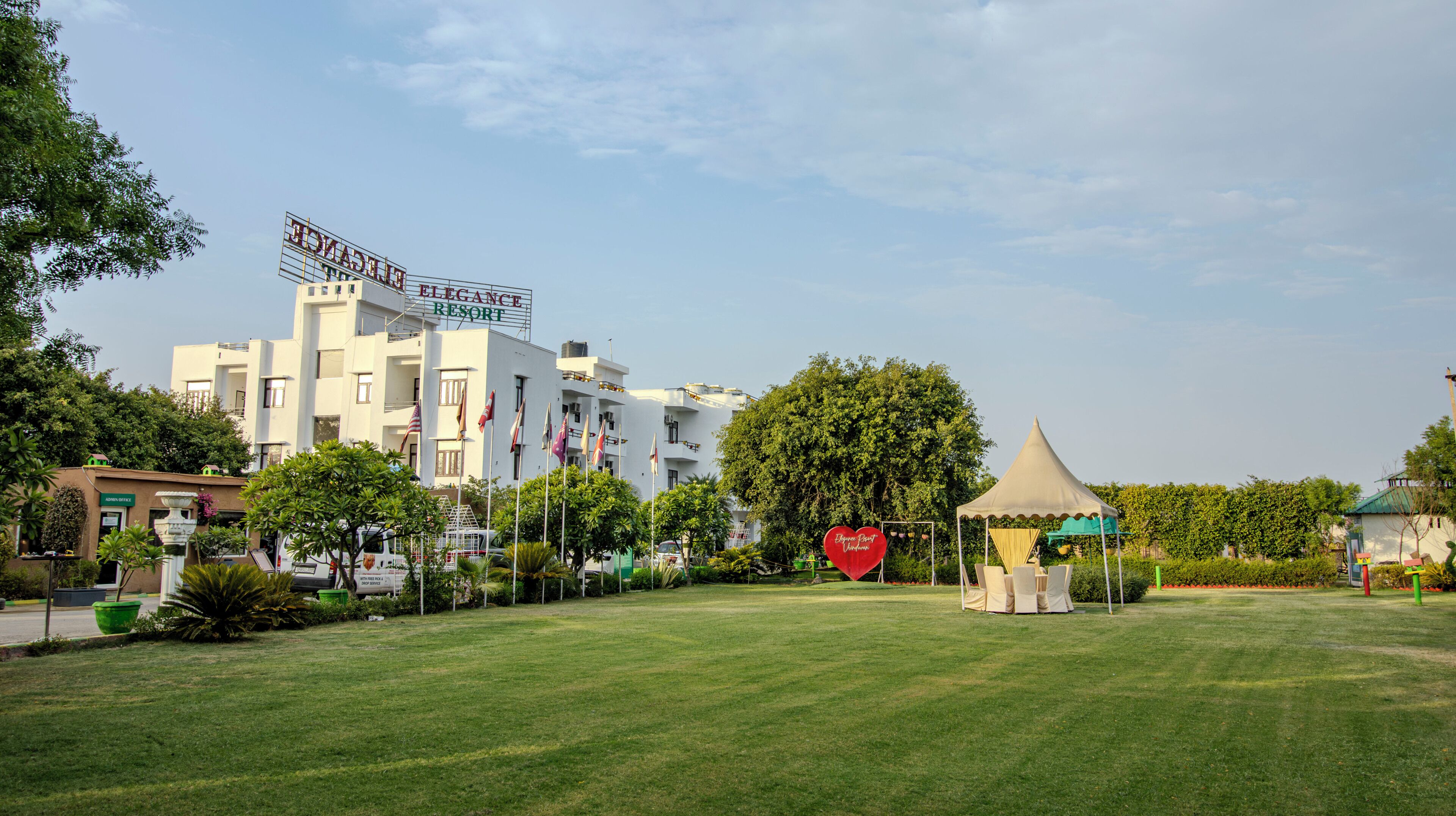 Un hôtel affichant une enseigne indiquant « Elegance Resort », entouré d’une pelouse bien entretenue et agrémenté d’un belvédère.