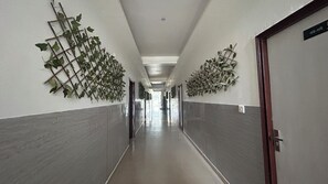 A corridor with a tiled floor, doors on both sides, and decorative foliage on the walls.