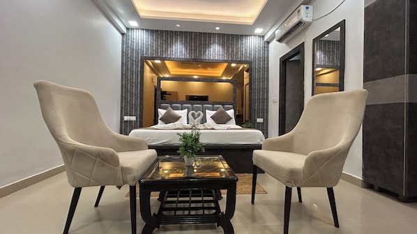 A modern bedroom with a large bed, two armchairs, a small table with a plant, and a mirror. - Elegance Resorts (Vrindavan)
