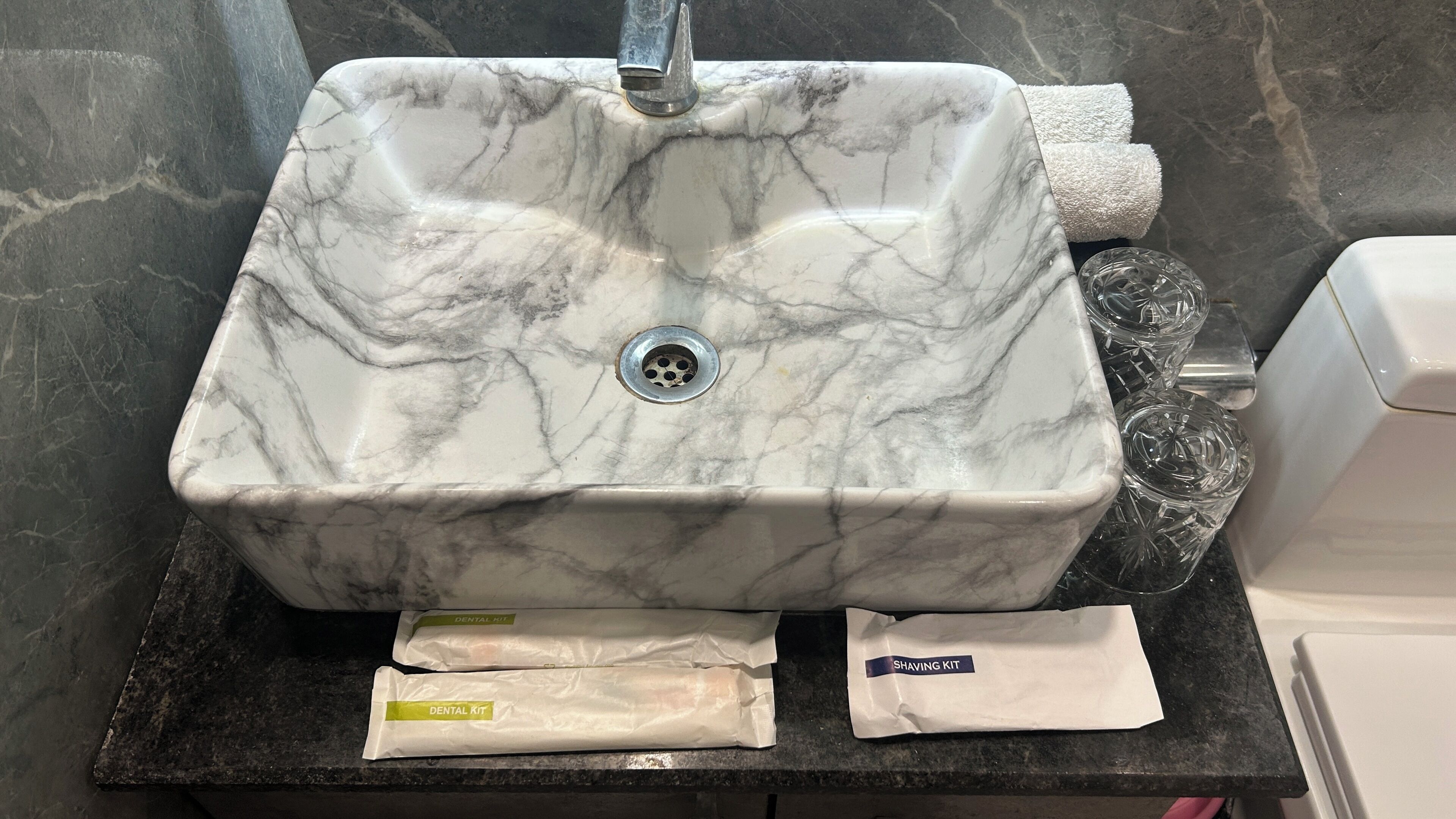 A bathroom sink with a marble countertop, a faucet, and two packages labeled 'Dental Kit' and 'Shaving Kit'.