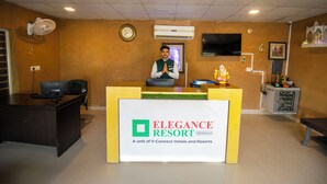 A reception desk at the Elegance Resort with a clock, air conditioning unit, and a TV on the wall. - Elegance Resort, Vrindavan (Vrindavan)