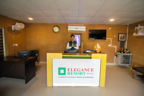 A reception desk at the Elegance Resort with a clock, air conditioning unit, and a TV on the wall. - Elegance Resort, Vrindavan (Vrindavan)