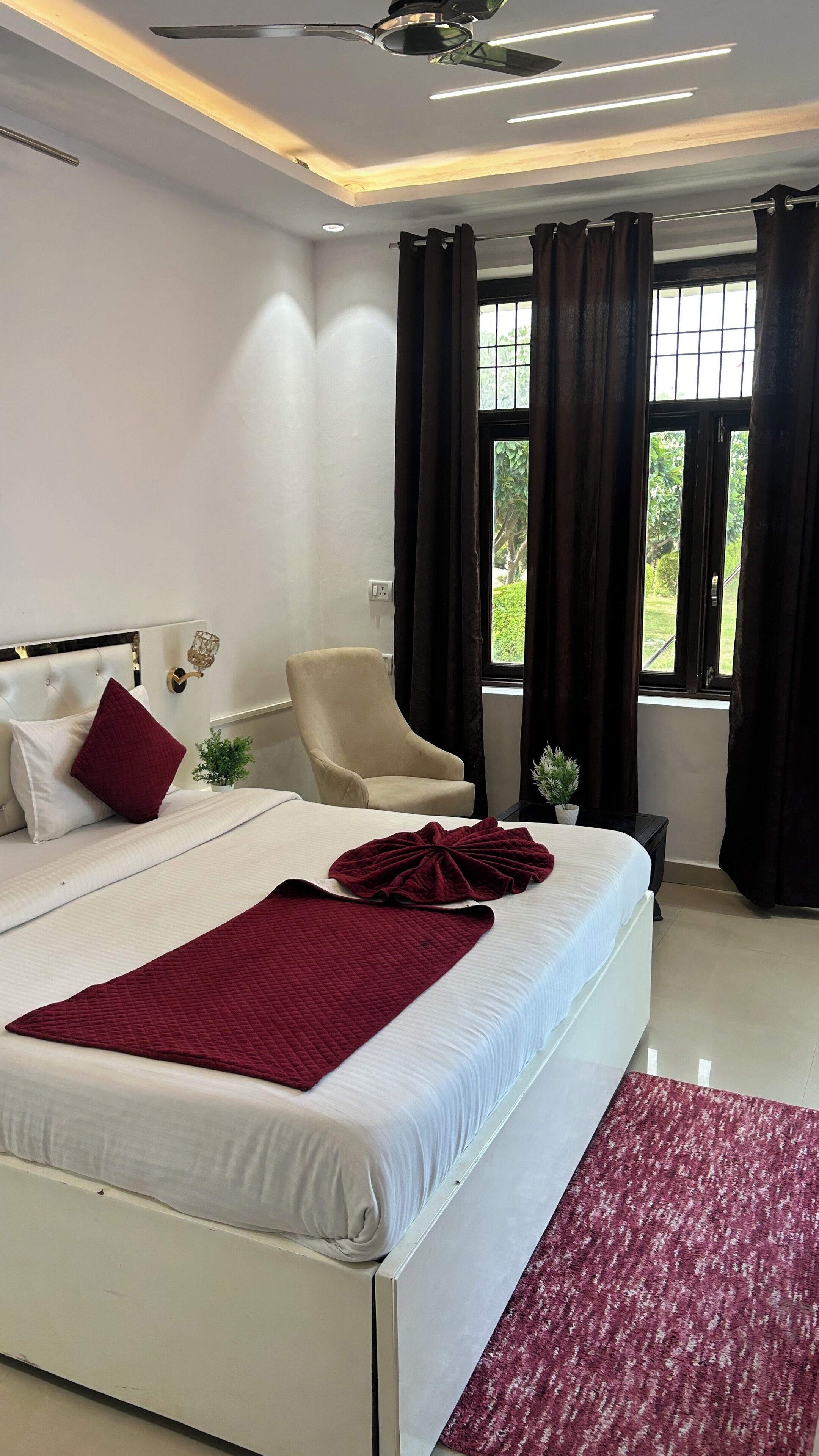A bedroom with a bed, a chair, a window with curtains, and a ceiling fan.