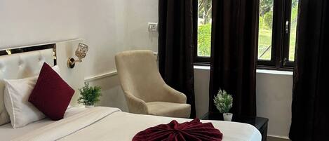 A bedroom with a bed, a chair, a window with curtains, and a ceiling fan.