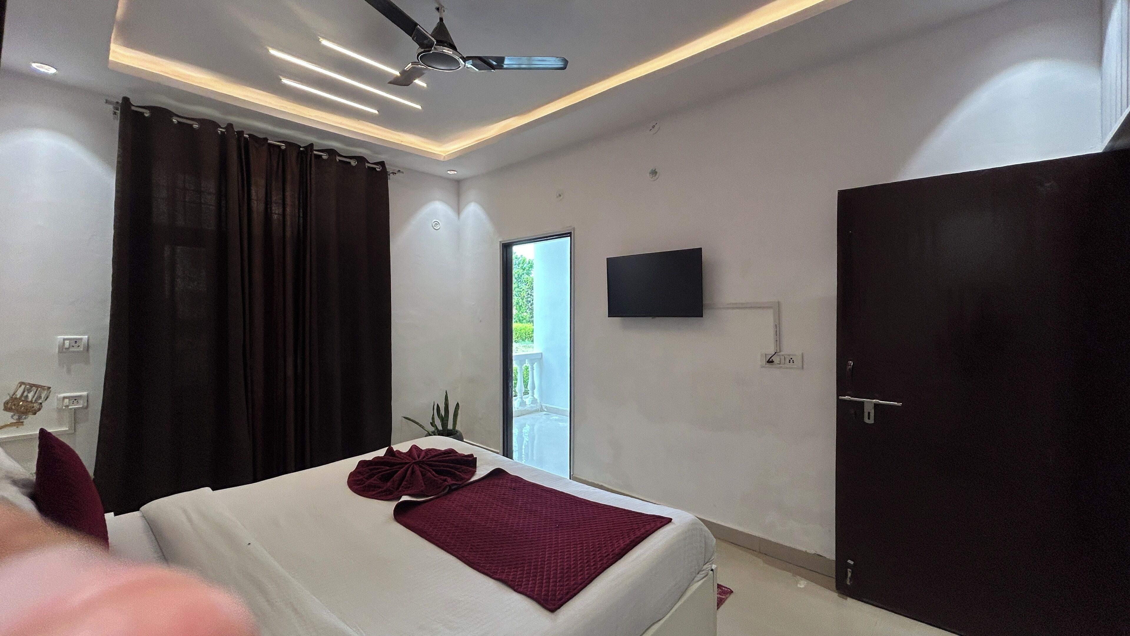 Un dormitorio moderno con cama, televisor de pantalla plana, ventilador de techo y puerta que da a un balcón.