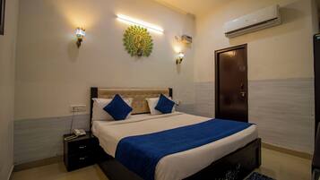 A hotel room with a bed, bedside tables, a telephone, wall-mounted lights, and an air conditioning unit.