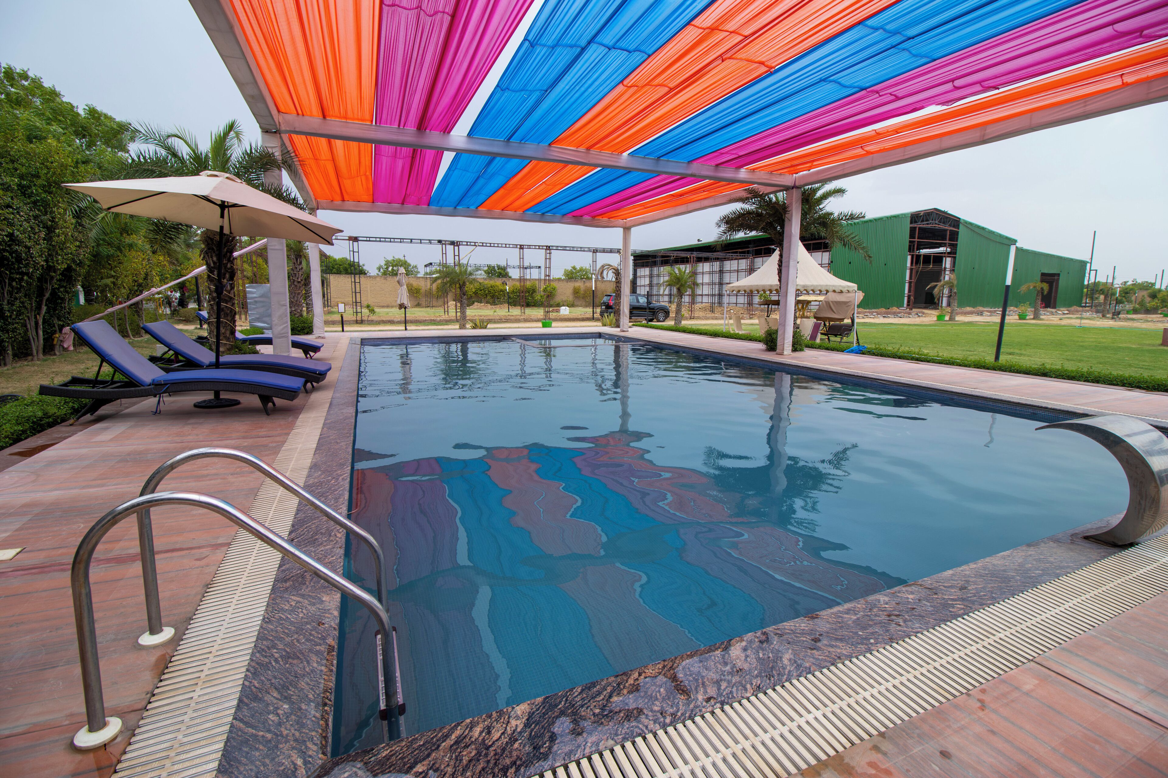 Una piscina con un toldo colorido sobre ella, rodeada de sillas de descanso y un área junto a la piscina.