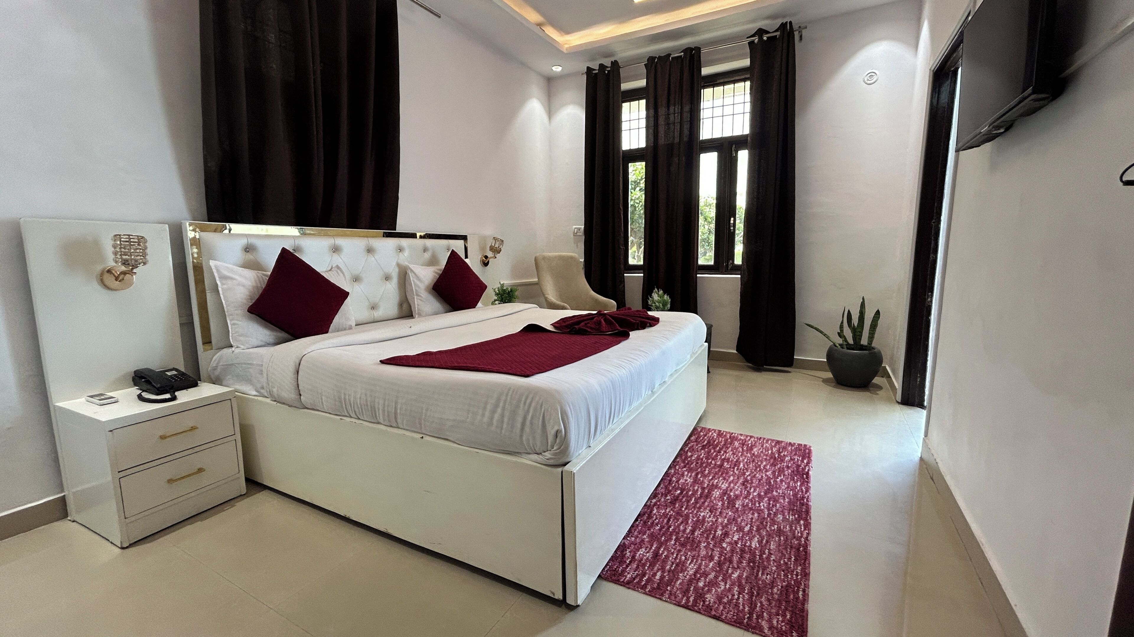 A modern bedroom with a large bed, bedside tables, a nightstand, a potted plant, and a window with curtains.