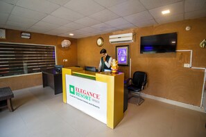A reception desk with a sign for 'Elegance Resort' and a clock on the wall.