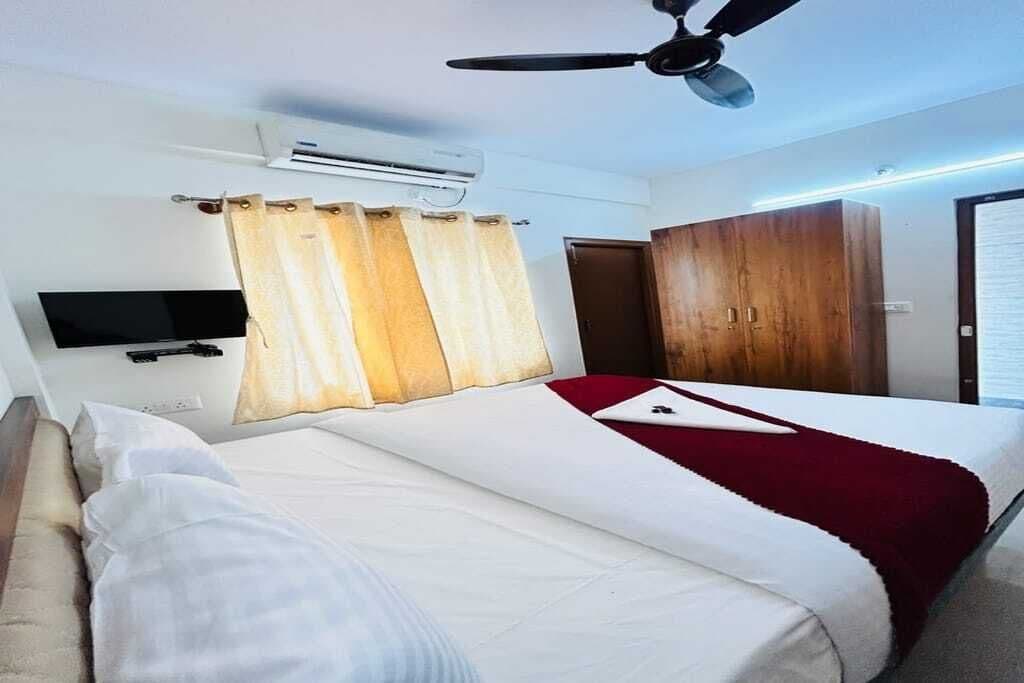 A hotel room with a bed, a television, an air conditioning unit, a ceiling fan, and a wardrobe.