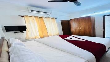 A hotel room with a bed, a television, an air conditioning unit, a ceiling fan, and a wardrobe.