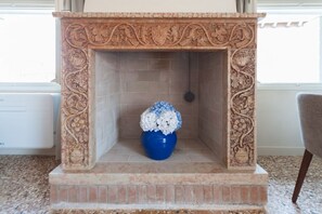 A fireplace with intricate carvings and a blue vase with white flowers. - Elegance and comfort in the heart of Venice – Canal view in San Marco (Venice)