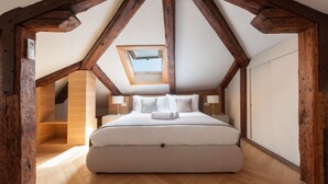 Ein Schlafzimmer mit schrägen Wänden, Holzbalken, einem Oberlicht, einem Bett mit Kissen und einem Nachttisch.