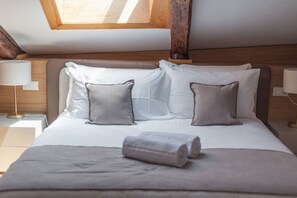 Ein ordentlich bezogenes Bett mit Kissen und einem zusammengerollten Handtuch, eine Nachttischlampe und ein hölzernes Kopfteil.