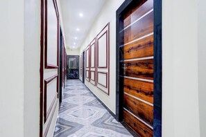 A hallway with patterned flooring, a wooden door with horizontal stripes, and a series of framed windows along the wall. - Super OYO Collection O Subedarganj (Prayagraj)